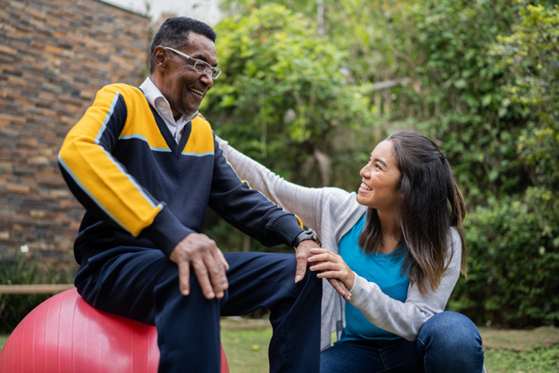 caregiver assisting senior man on excercise ball